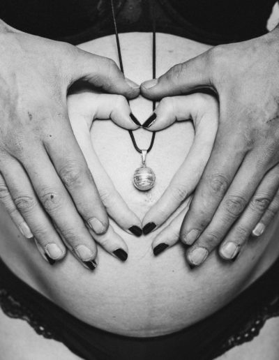 Les futurs parents forment un cœur sur le ventre de la future maman, mettant en valeur le bola de grossesse - Photographe grossesse en Haute-Savoie