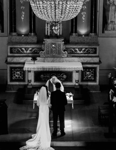 Cérémonie de mariage : les mariées font face au prêtre sous le somptueux lustre de l'église.