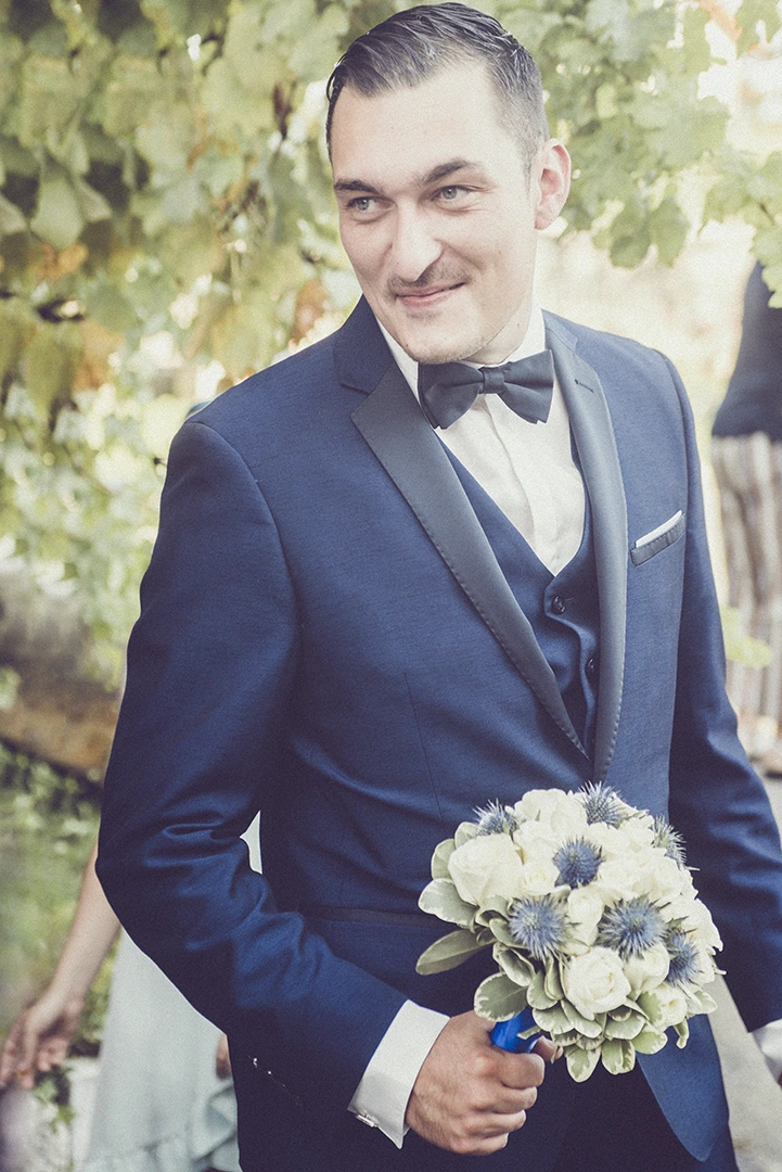 Portrait souriant du marié tenant fièrement le bouquet de sa femme dans son costume élégant, lors d'un moment de complicité.