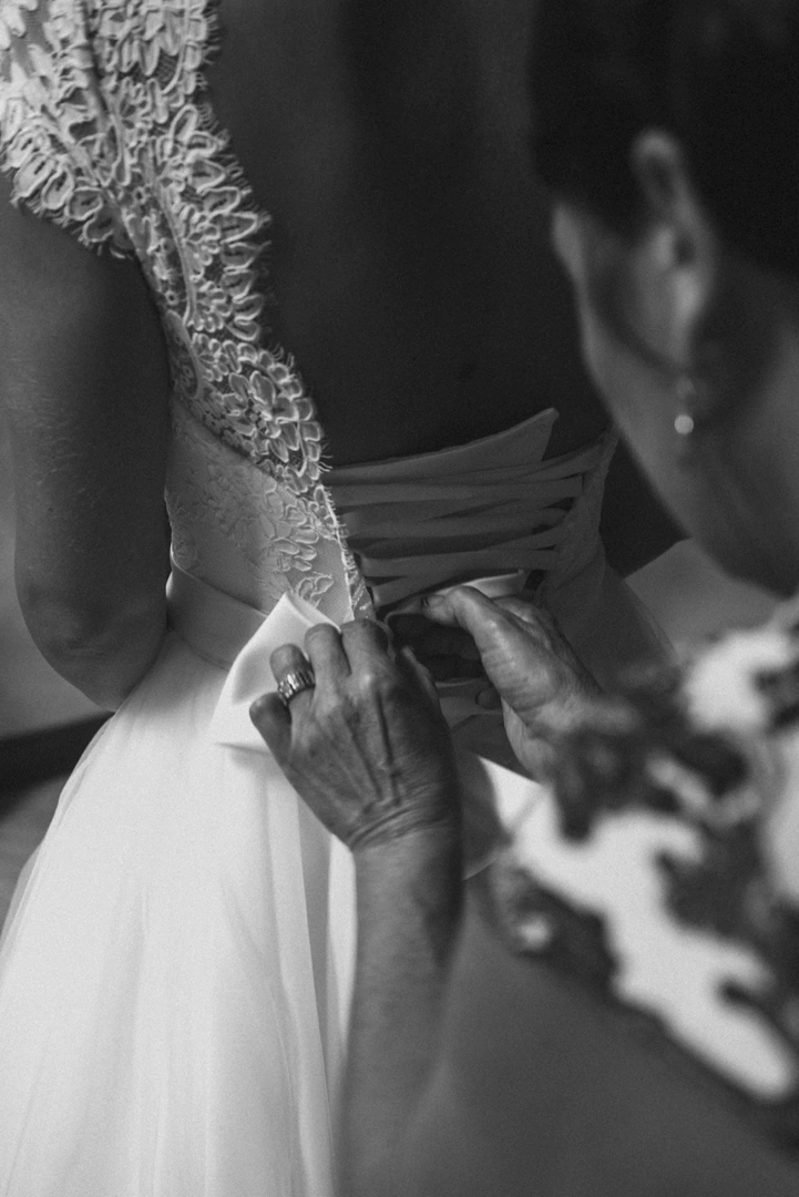 Moment intime où la mère de la mariée aide à nouer la robe de sa fille pendant les préparatifs du mariage, capturé dans une atmosphère pleine d'émotion et de tendresse.