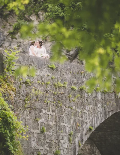 Deux jeunes mariées s'embrassent passionnément sur un pont en pierre à Cluse