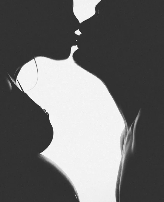 Photo d'un couple de futurs parents s'embrassant sur la bouche, capturé en silhouette dans le style ombre chinoise. Une image romantique et artistique symbolisant l'amour et l'attente d'un bébé.