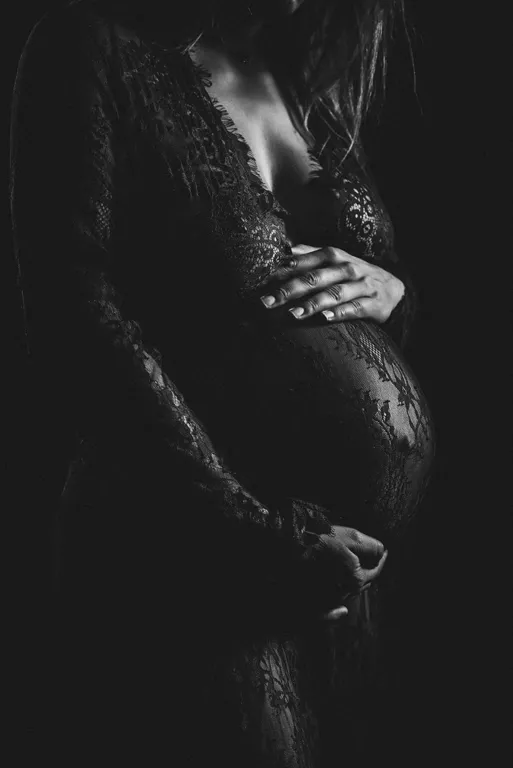 Photo en noir et blanc d’une future maman en studio à Sallanches, mettant en valeur la dentelle de sa robe et son ventre arrondi à travers un cadrage serré des épaules aux genoux.