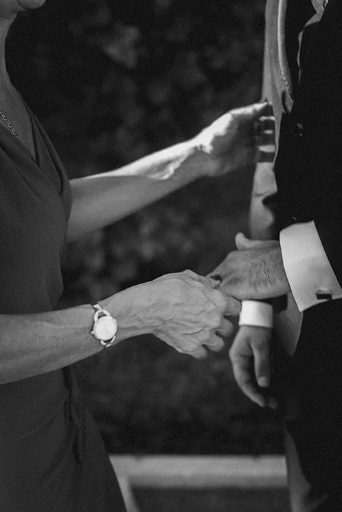 Lien intergénérationnel au mariage : La main de la grand-mère tenant celle de son petit-fils La main ridée d'une grand-mère tient tendrement la main de son petit-fils lors d'un mariage, symbolisant les liens intergénérationnels et la transmission familiale, pour une photo de mariage originale et émouvante.