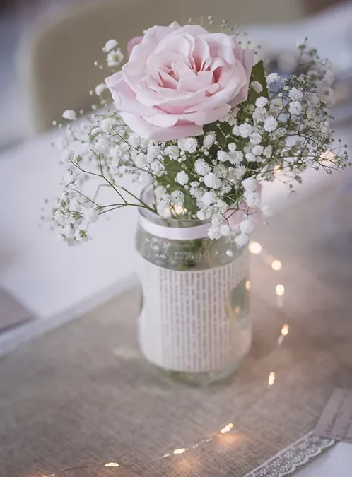 Décoration de mariage mettant en scène un bouquet de fleurs blanches et une rose, agrémentée d'une guirlande lumineuse pour une ambiance romantique et originale, idéale pour des photos uniques.