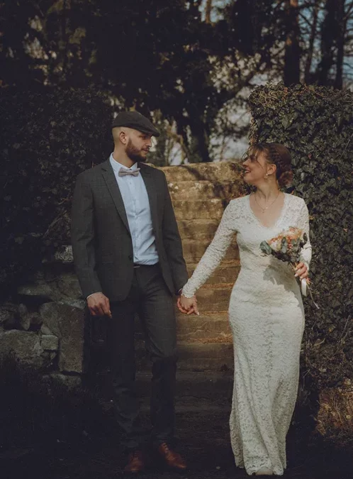 Les mariés marchent main dans la main en se regardant avec un sourire après la cérémonie de mariage. Photographie de mariage authentique et naturelle.