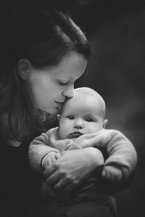 Tendresse maternelle : Maman et son bébé lors d'une séance photo en extérieur Une maman tenant son bébé dans ses bras et rapprochant sa tête de lui lors d'une séance photo en extérieur. Le bébé regarde directement le photographe.