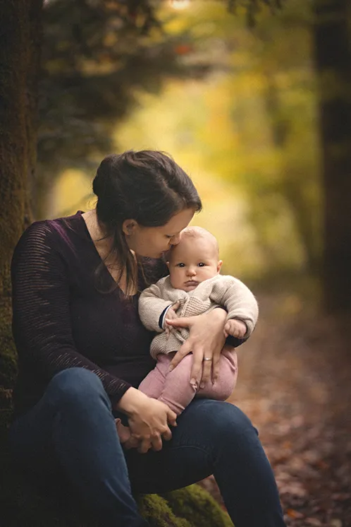 Photographe famille Haute-Savoie : Moment de tendresse entre une mère et son enfant en forêt Portrait d'une mère donnant un baiser à son bébé dans un cadre forestier en Haute-Savoie.