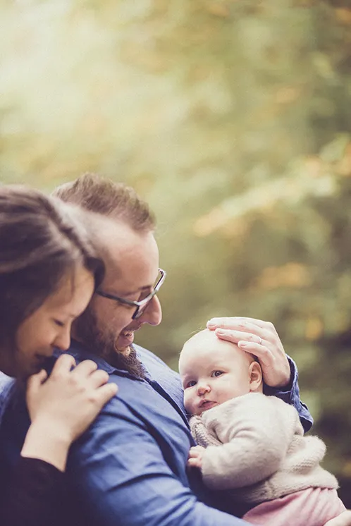 Photographe famille Haute-Savoie : Moment de complicité entre parents et bébé en forêt Photographe famille Haute-Savoie : une scène touchante avec les parents et leur bébé en forêt.