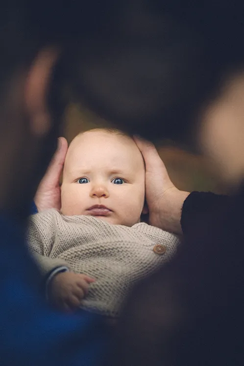 Séance photo de famille en Haute-Savoie : Parents et bébé en forêt, regard vers le photographe Les parents se sont approchés l'un de l'autre, encadrant le visage de leur bébé qui regarde le photographe, lors d'une séance photo de famille en forêt en Haute-Savoie.