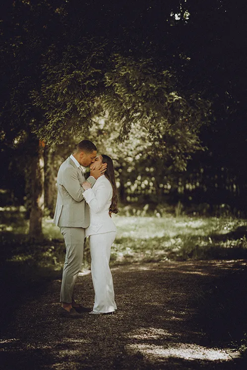 Séance photo de couple après la cérémonie de mariage à Genève : un tendre baiser à l'ombre des arbres Photographie d'un couple échangeant un baiser tendre lors de leur séance photo de mariage dans un parc ombragé de Genève, après leur union civile.