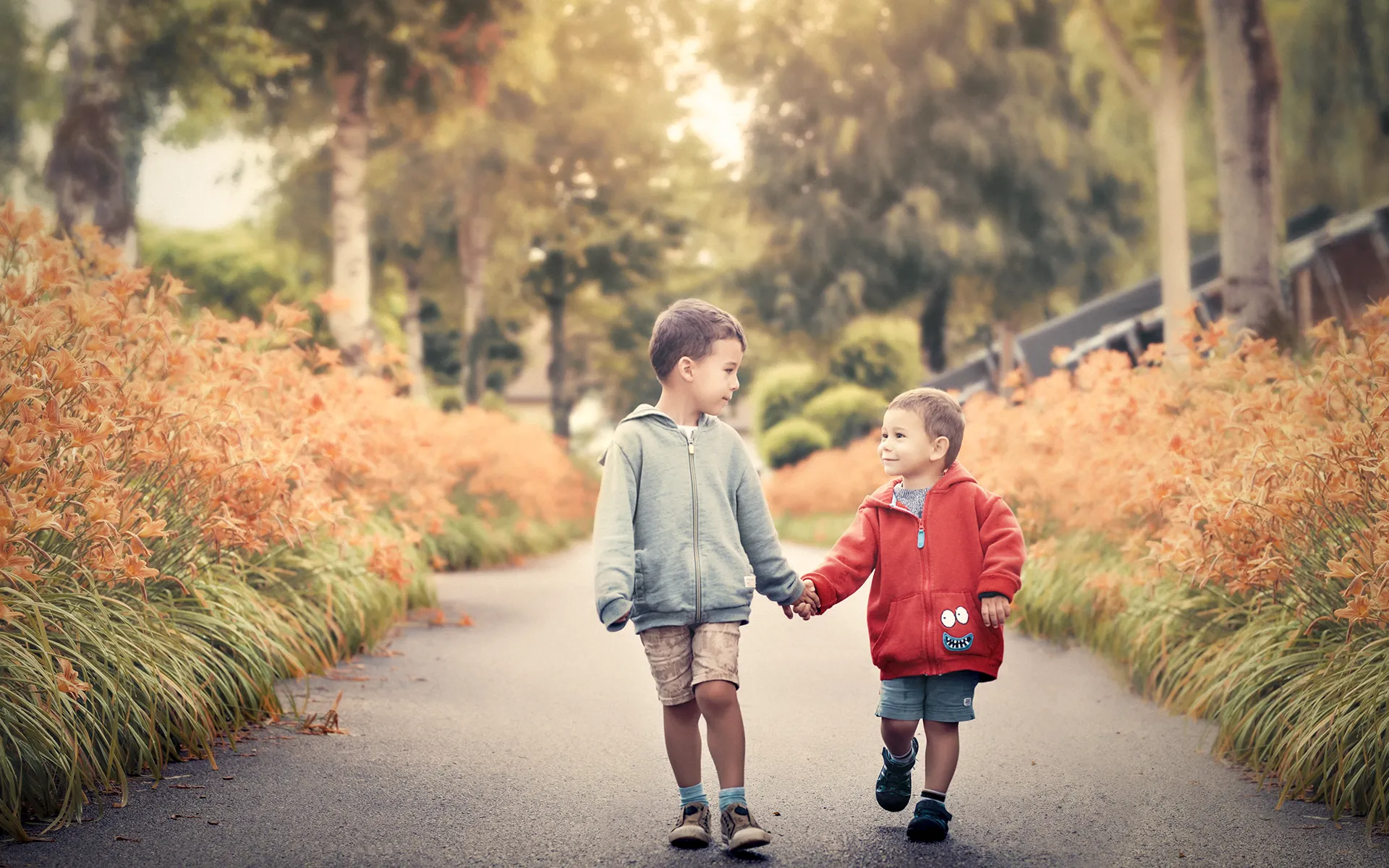Séance photo famille en Haute-Savoie : Deux enfants partagent un moment de complicité dans une allée fleurie Deux jeunes enfants marchent main dans la main en se regardant tendrement dans une allée de fleurs lors d'une séance photo de famille en Haute-Savoie. Cette image capture la complicité et l'innocence de l'enfance dans un cadre naturel et fleuri.