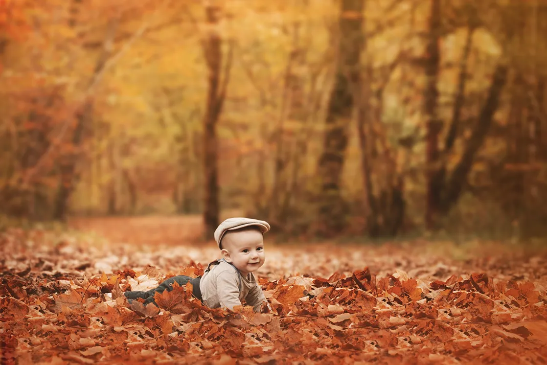 Photographe famille Haute-Savoie : Bébé dans un décor automnal Un bébé allongé dans un tas de feuilles d'automne lors d'une séance photo de famille en Haute-Savoie.