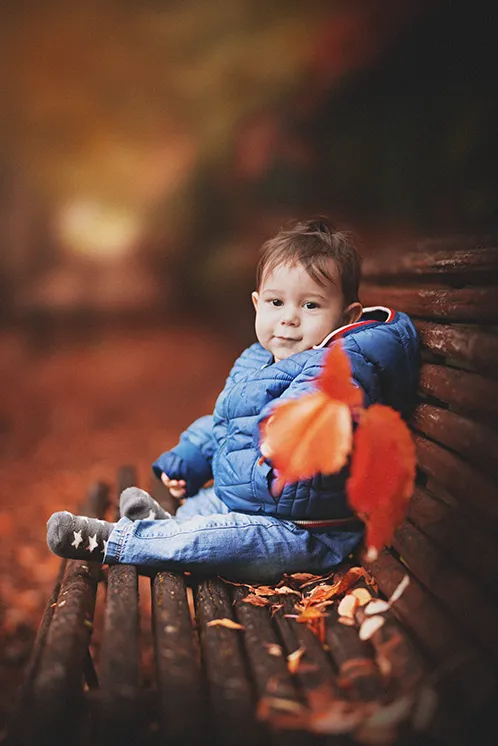 Séance photo famille ludique en Haute-Savoie : Bébé partage un moment complice avec le photographe Photographie d'un bébé offrant une feuille d'automne pendant une séance photo famille ludique en Haute-Savoie. L'image met en valeur la connexion sincère entre l'enfant et le photographe, reflétant l'approche basée sur le jeu et la spontanéité.